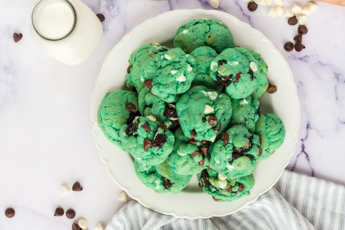 A plate of green cookies with chocolate chips and white chips, accompanied by a glass of milk on a marble countertop, showcases delightful cookie recipes.