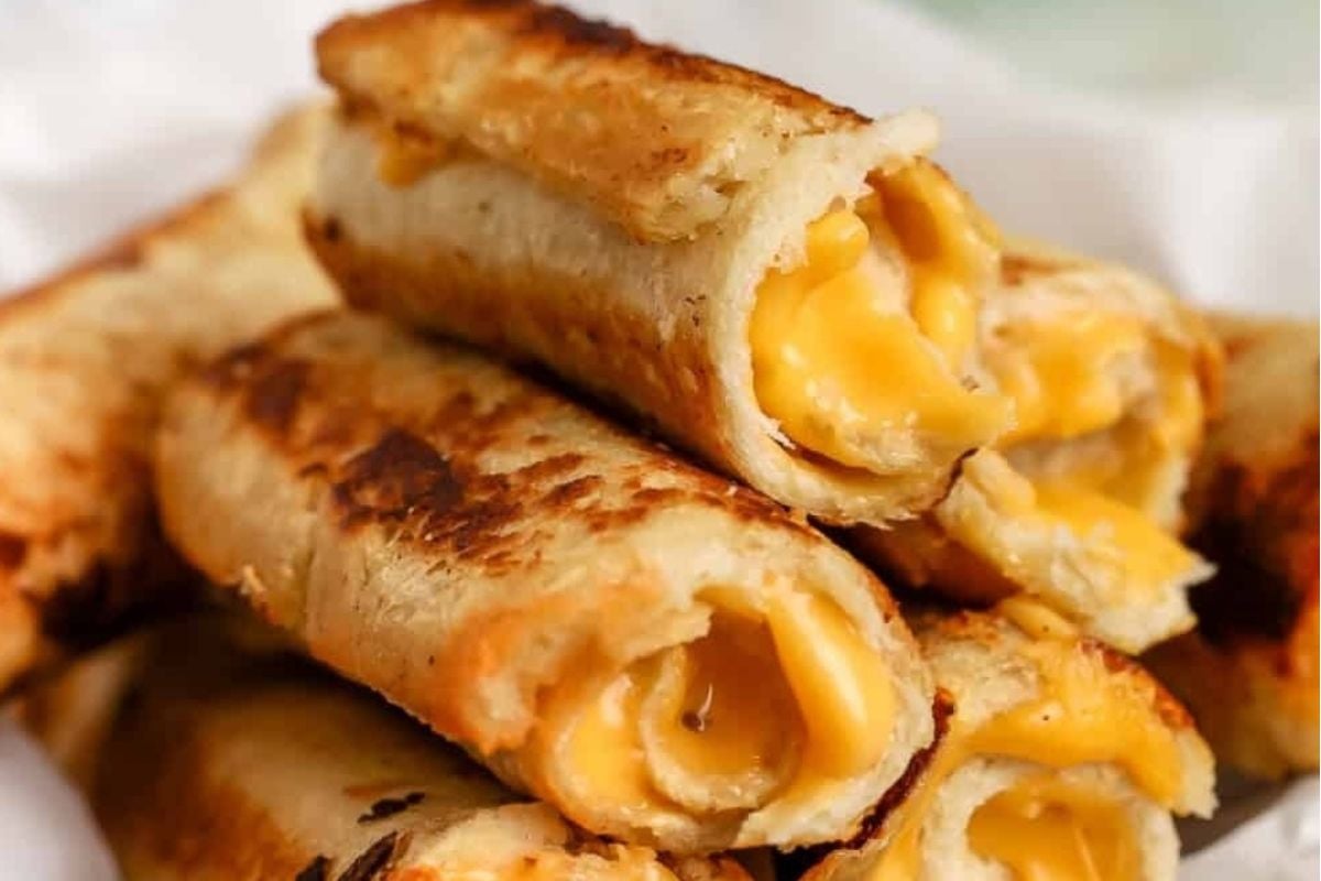 Close-up of cheesy recipes: crispy rolled tortillas filled with melted cheese on a white plate.