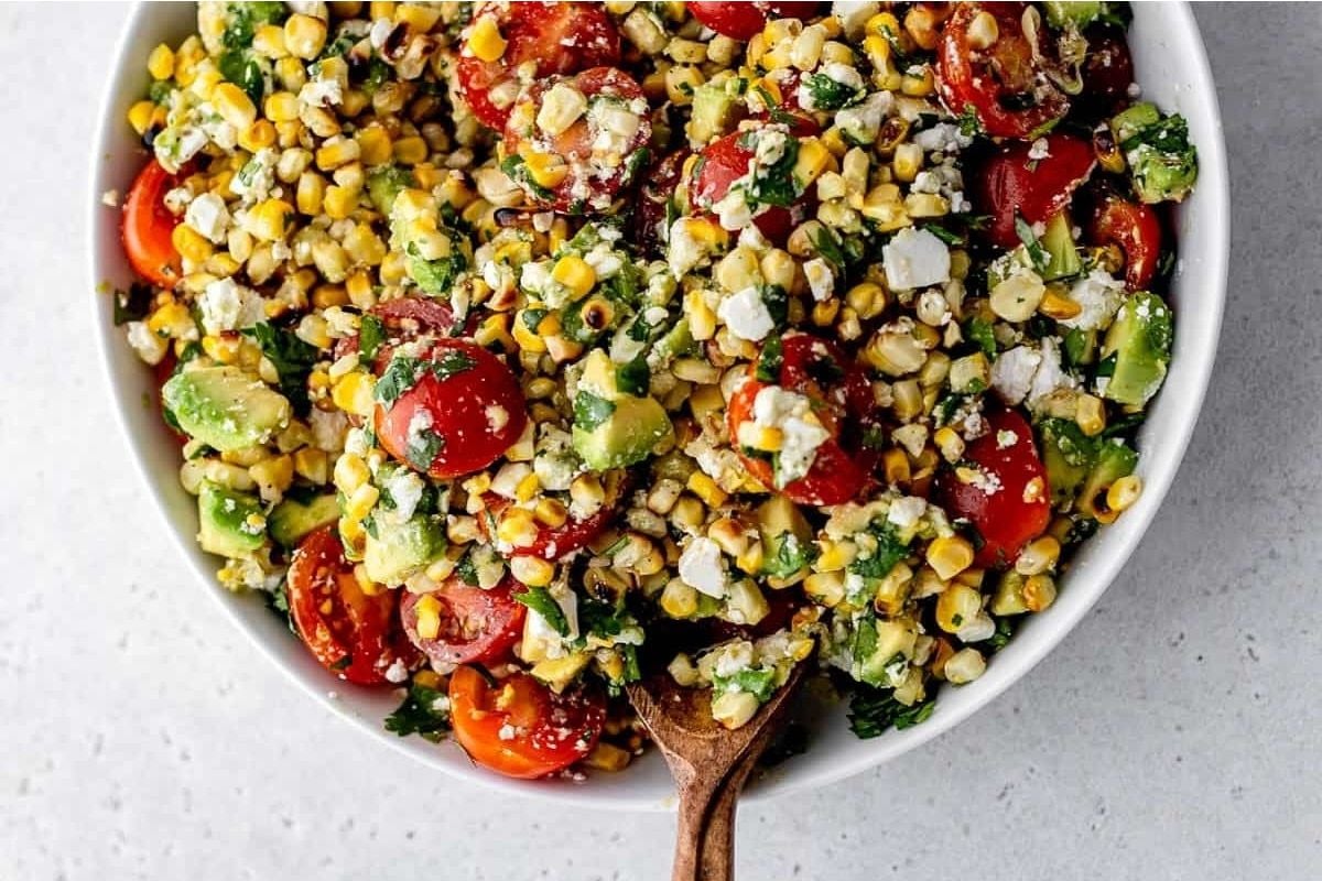 A bowl of corn salad with tomatoes and avocado, perfect for potluck sides.