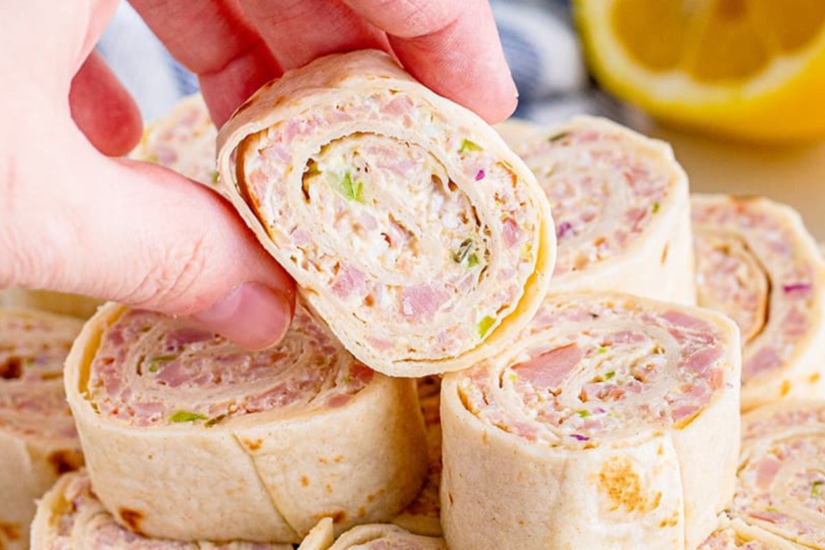 A hand picking up a ham and cream cheese pinwheel among other similar appetizers from Pinwheel Recipes.