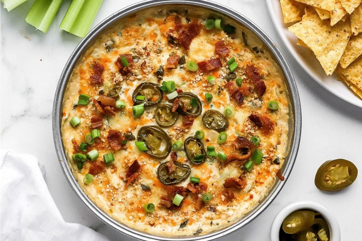 A bowl of cheesy dip with bacon and celery, perfect for potluck sides.