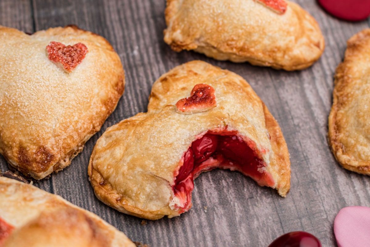 Heart-shaped pastries with fruit filling from pie recipes on a wooden surface.
