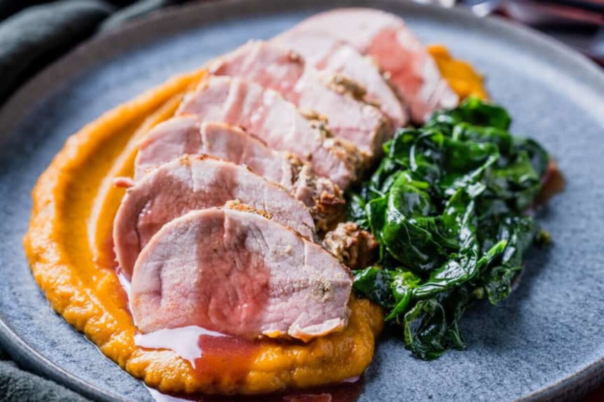 Sliced pork tenderloin served over a bed of pureed carrots with a side of saut&eacute;ed spinach on a ceramic plate for Easter dinner.