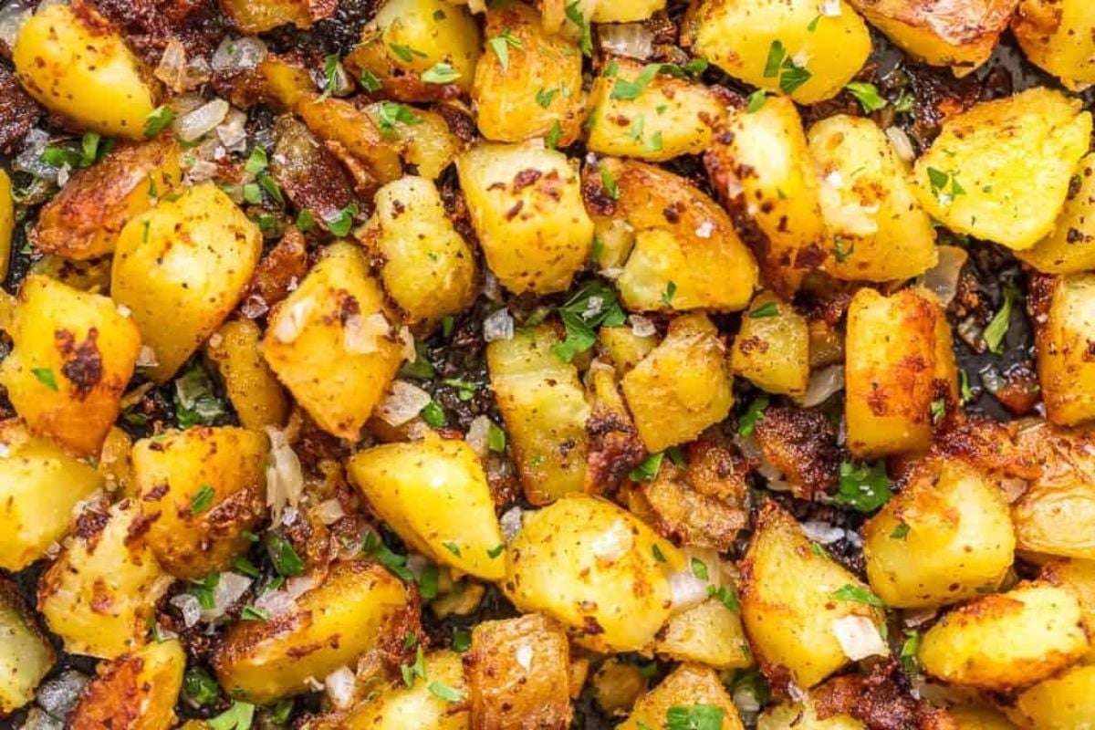 Close-up of seasoned, roasted potato cubes sprinkled with chopped herbs and small pieces of onions.