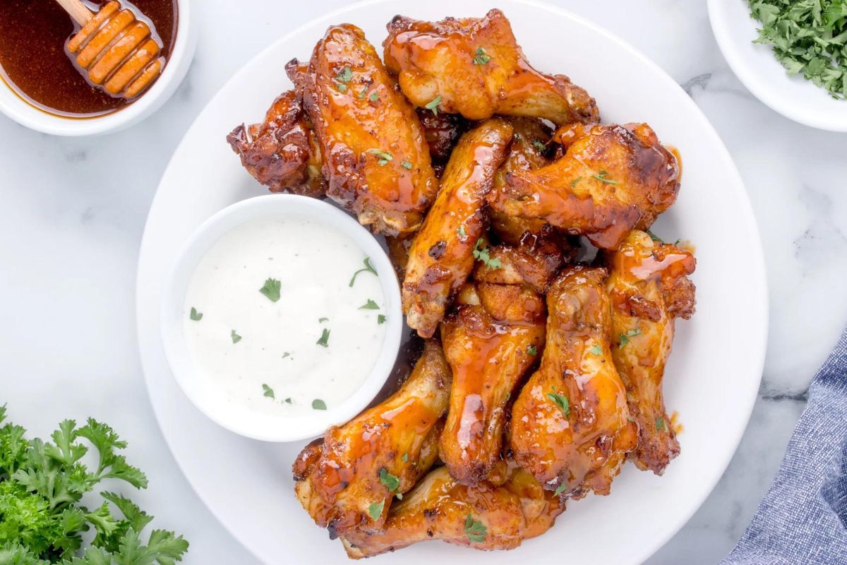 A plate of glazed chicken wings served with a side of ranch dressing.