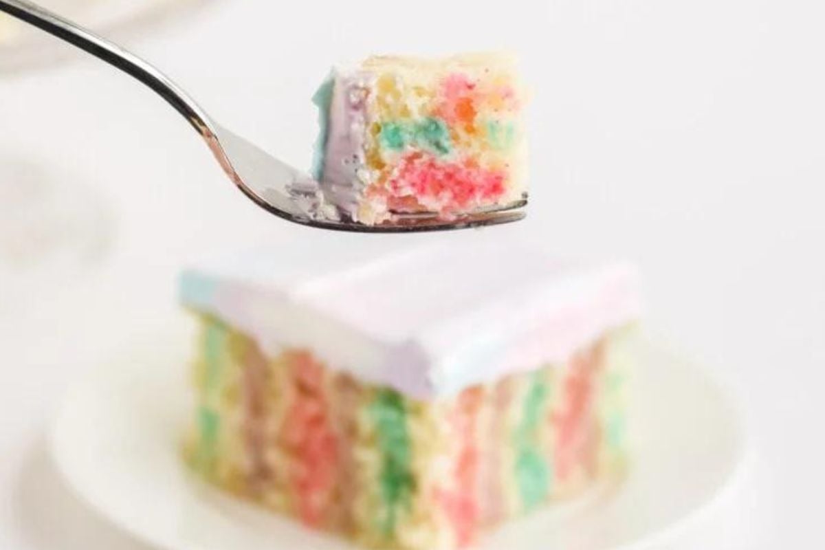 A forkful of colorful layered Jello cake with a slice on a plate in the background.