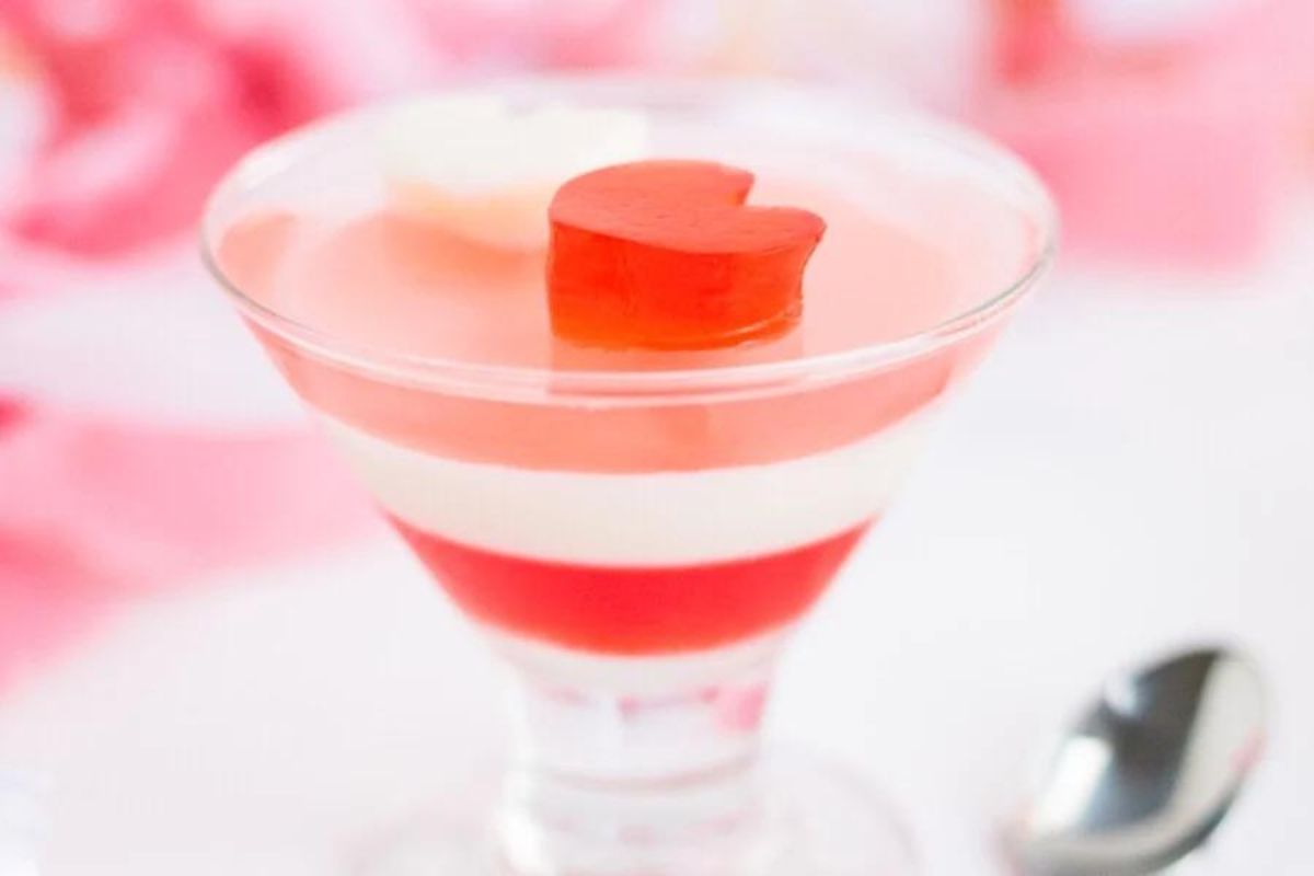 Layered Jello dessert in a glass with a heart-shaped garnish on top.