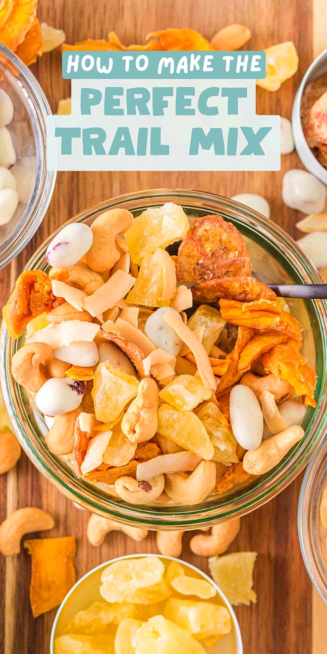 A jar of trail mix with nuts, dried fruit, and yogurt pieces, surrounded by small bowls on a wooden surface.