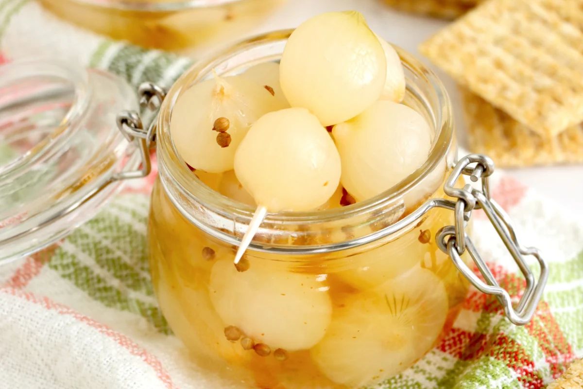 A jar of pickled onions with mustard seeds and a checked cloth in the background, perfect for those who love pickled recipes.