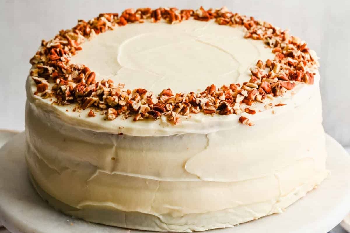 A layer cake with cream frosting topped with chopped nuts.