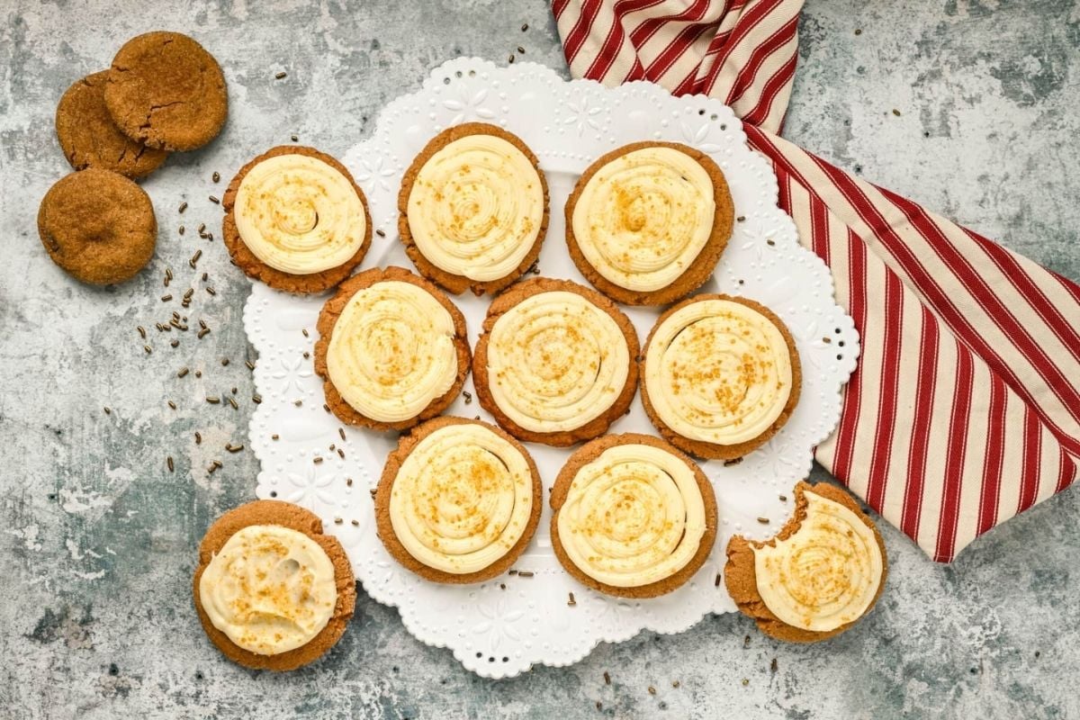 A plate of frosted cookies sprinkled with spices from various cookie recipes, next to a striped napkin and additional cookies on a textured surface.