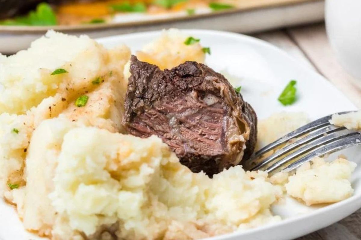 A plate with mashed potatoes and a slice of easy rib beef.