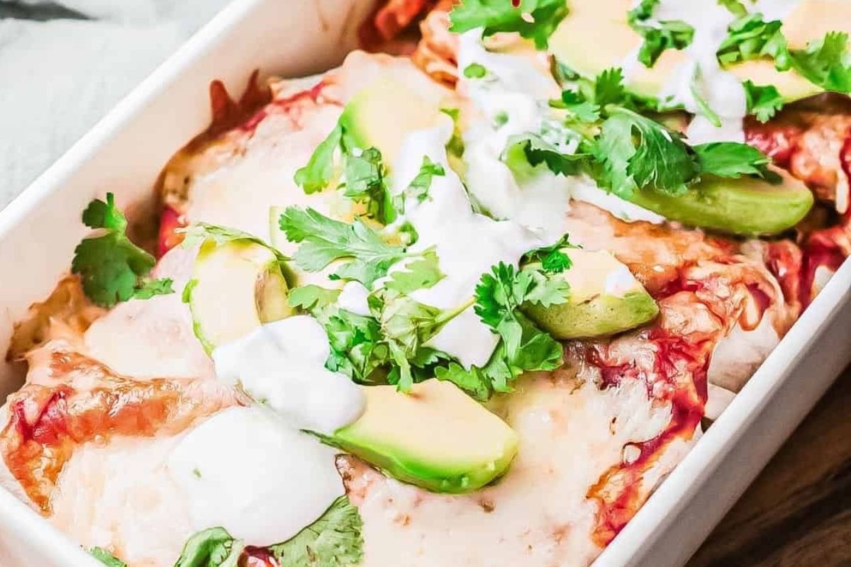 Baked enchiladas with a pizza flavored twist, topped with melted cheese, avocado slices, cilantro, and drizzled with sour cream.