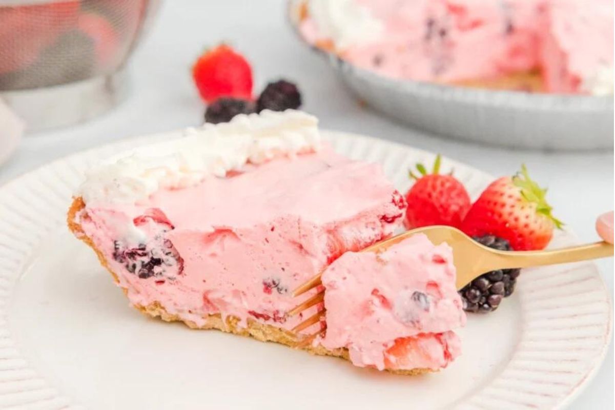 A slice of berry-flavored Jello cream pie on a plate with a fork, garnished with fresh berries.