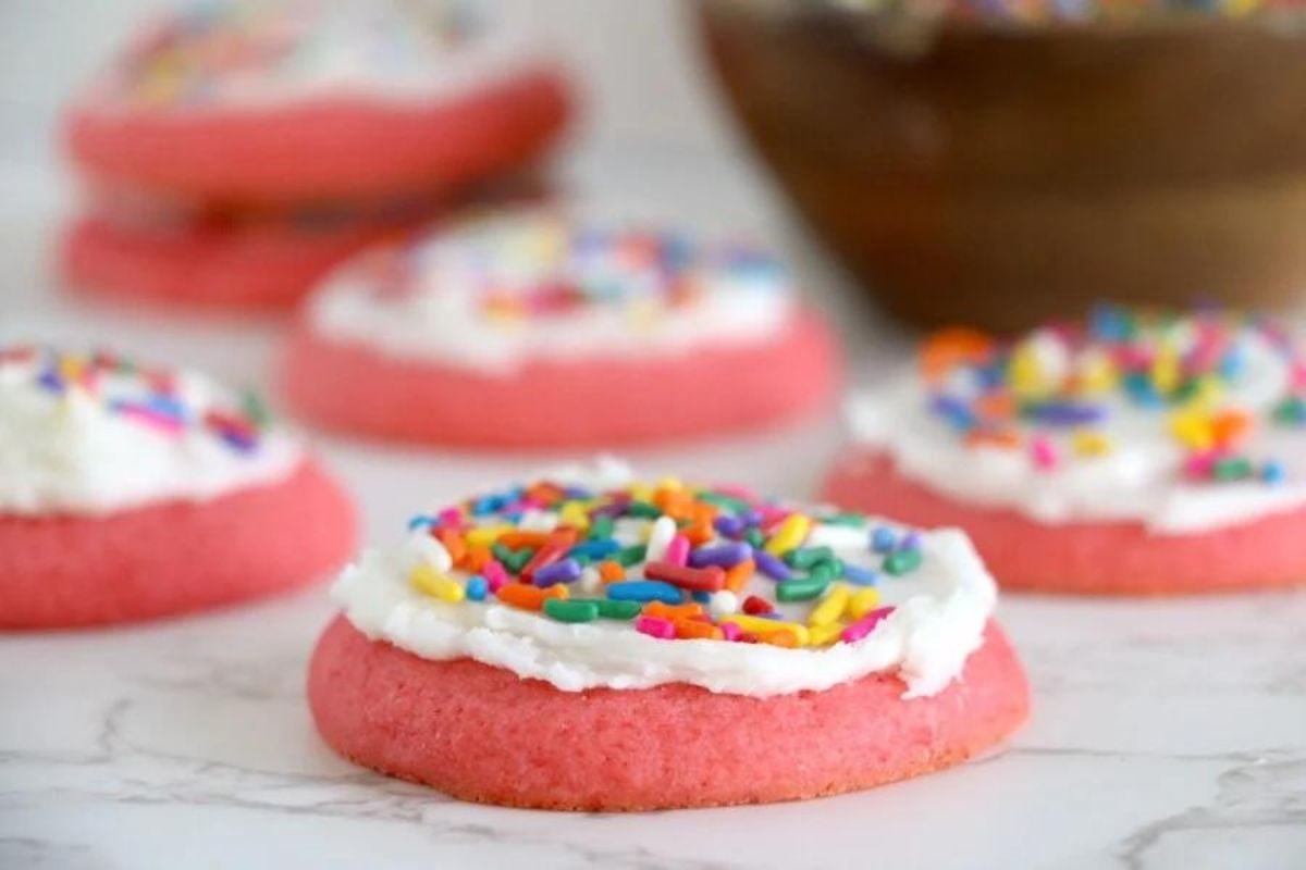 Rows of pink Jello frosted cookies topped with colorful sprinkles.