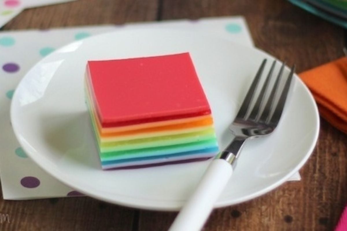 Rainbow jello salads on a plate with a fork.