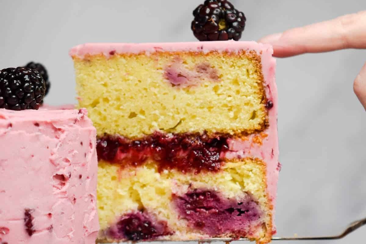 A slice of layered berry layer cakes with pink frosting and a finger poking it.