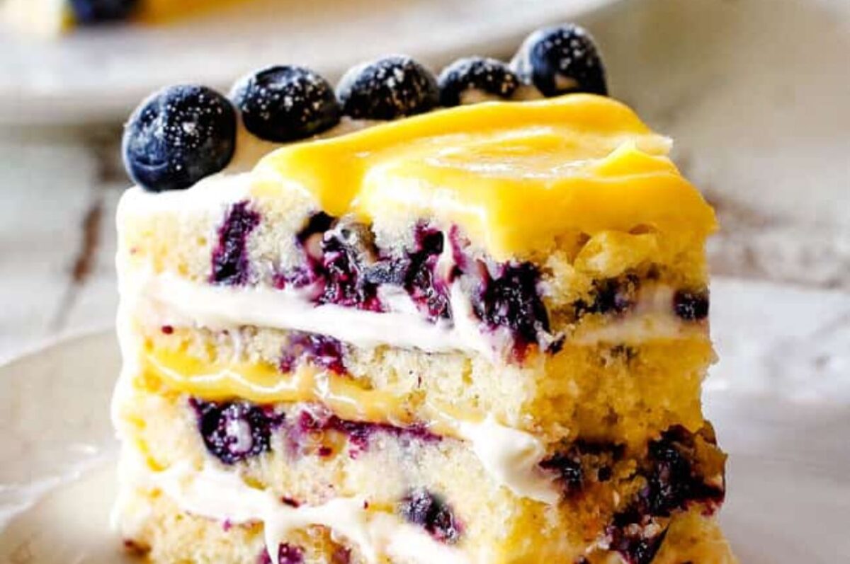 A slice of Easter lemon blueberry cake with creamy frosting and fresh berries on top.