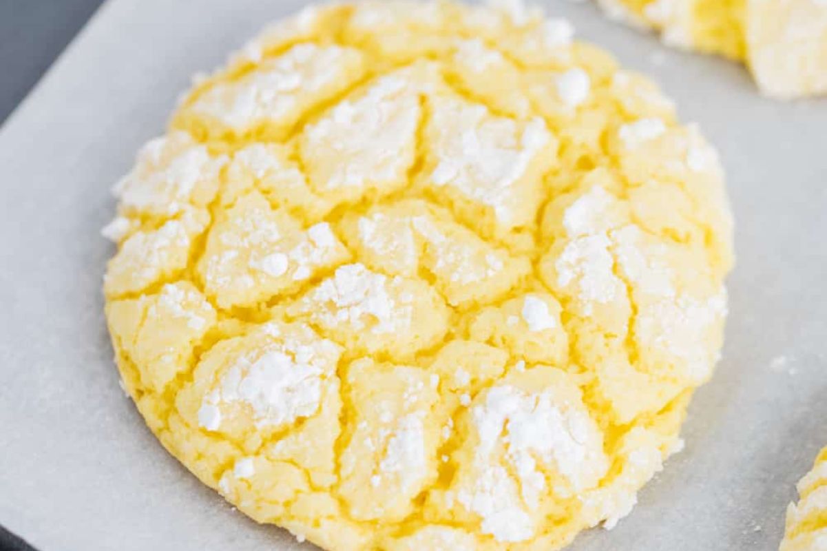 A close-up of a freshly baked Easter crinkle cookie with powdered sugar on parchment paper.