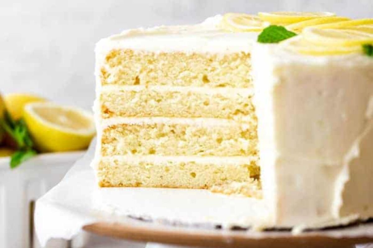 An Easter lemon layer cake with white frosting on a plate, garnished with lemon slices and mint leaves.