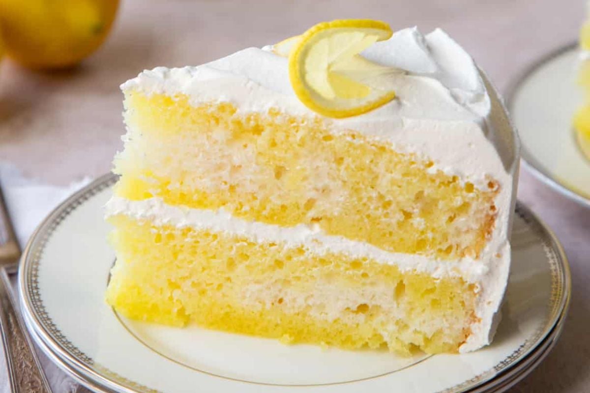 An Easter dessert: a slice of lemon cake with creamy frosting and a thin lemon slice garnish on a white plate.