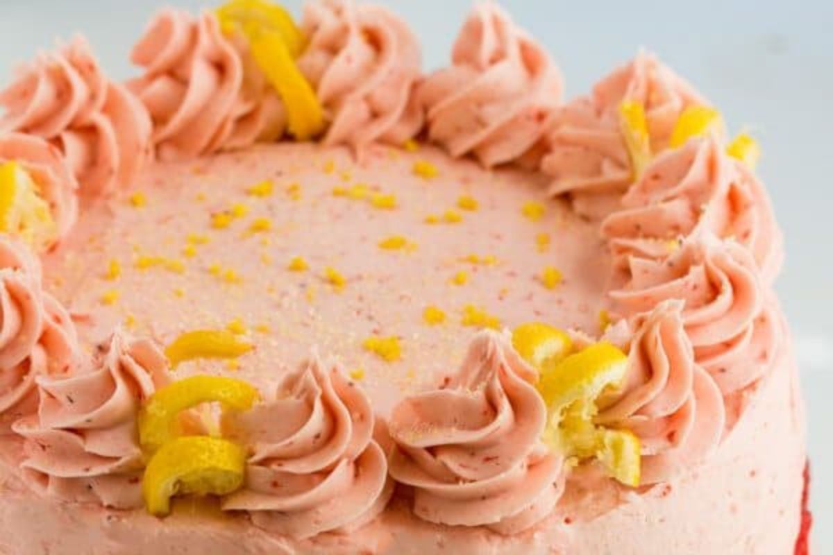 An Easter pink frosted cake with yellow sprinkle accents and decorative piping on the edge.