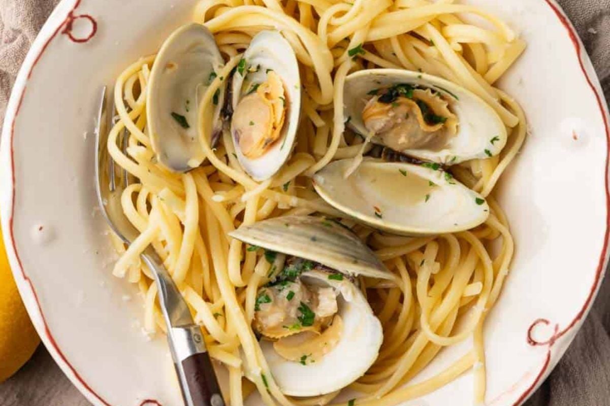 A plate of spaghetti alle vongole, featuring linguine pasta and clams garnished with parsley from our seafood recipes, served with a lemon wedge on the side.