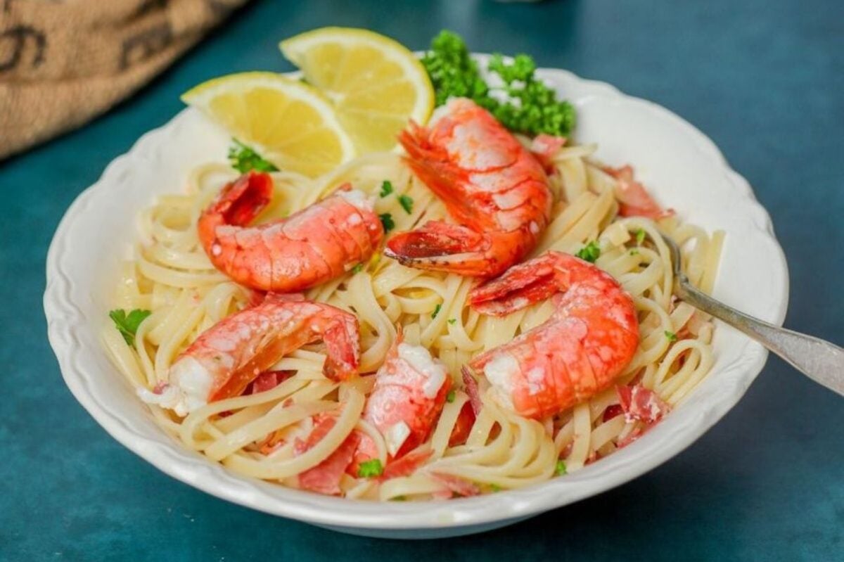 A bowl of shrimp linguine from our seafood recipes, garnished with lemon slices and parsley, served on a blue tablecloth.