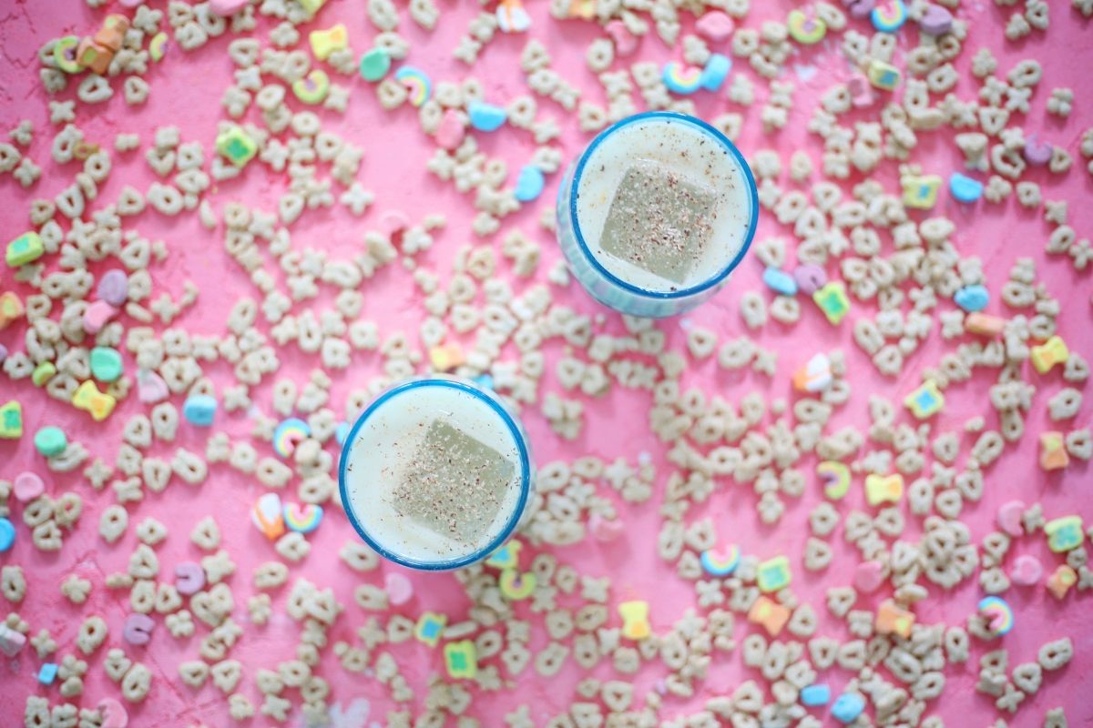 Two cups of cereal featuring recipes using Lucky Charms on a pink background.