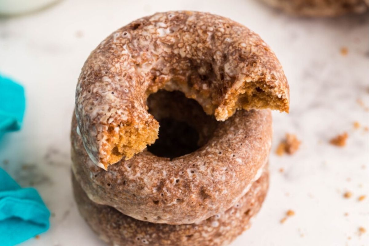 A stack of two whole-grain donuts, with the top one having a bite taken out, on a light-colored surface with crumbs scattered around.