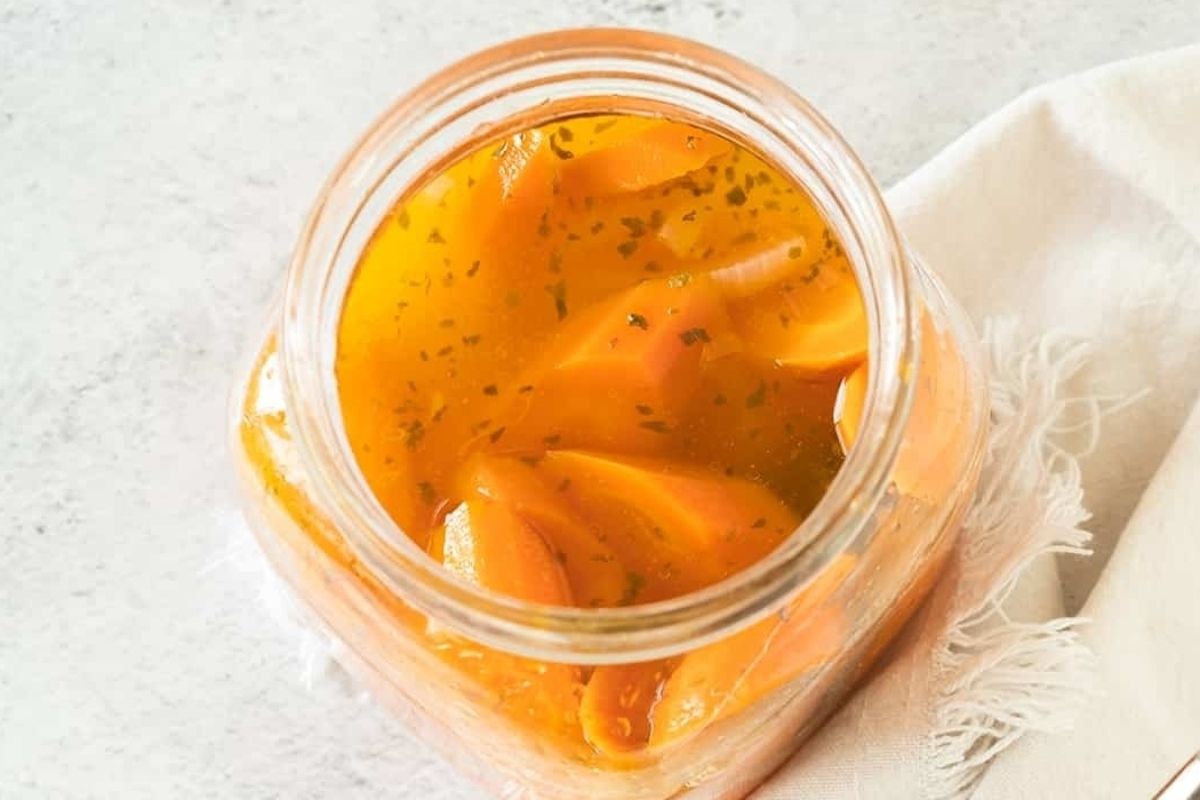A jar of preserved sliced oranges with herbs following pickled recipes.
