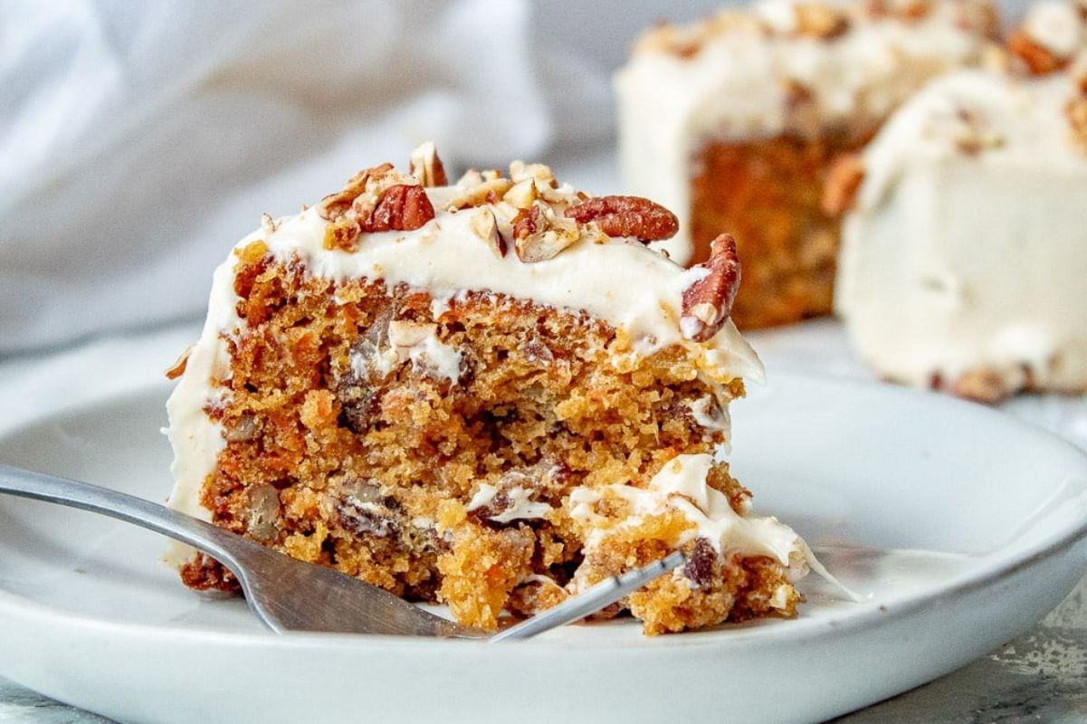 An Easter carrot cake slice with cream cheese frosting and chopped nuts, served on a white plate with a fork.
