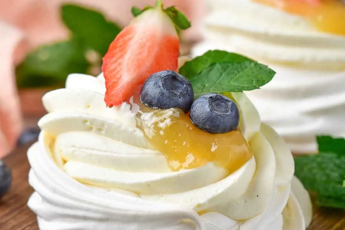 Easter mini pavlovas topped with fresh cream, lemon curd, strawberries, and blueberries.