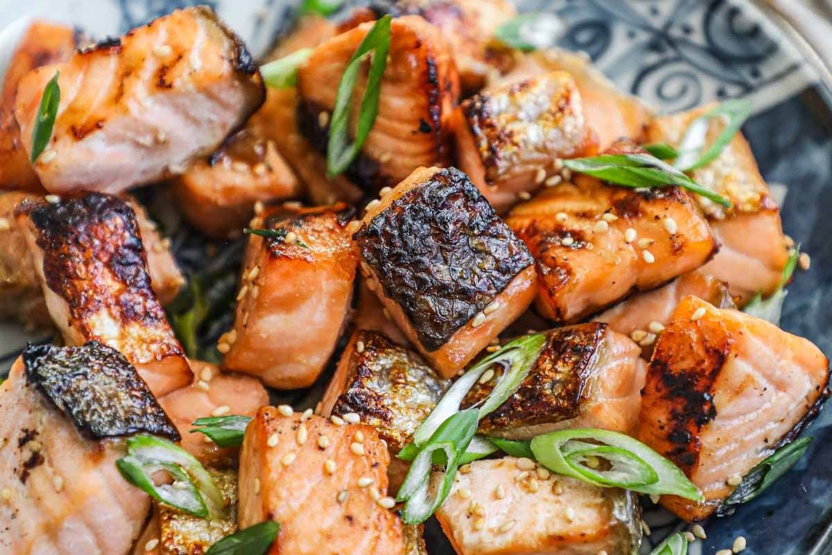 Grilled salmon cubes garnished with sesame seeds and sliced green onions, served on a decorative plate as part of our seafood recipes.