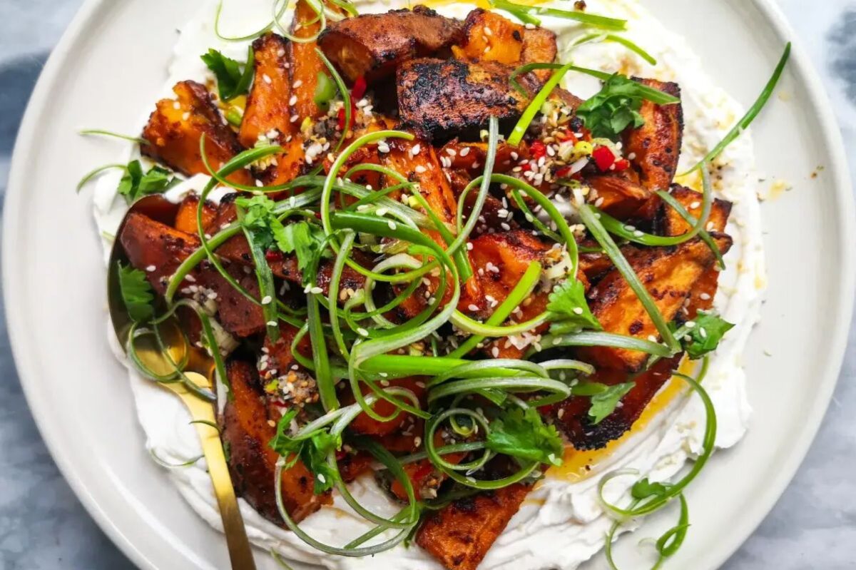 Roasted sweet potatoes served over a creamy base and garnished with scallions, herbs, and sesame seeds, perfect for Easter sides.