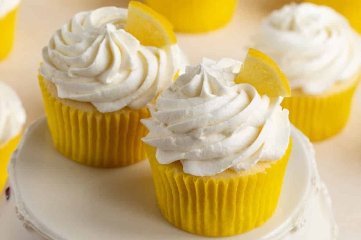 A potluck dessert featuring cupcakes with white frosting and lemon wedges.