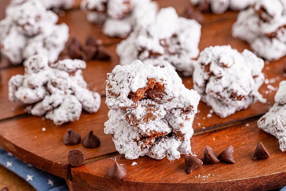 Powdered sugar-coated chocolate cookie recipes on a wooden board, surrounded by chocolate chips.