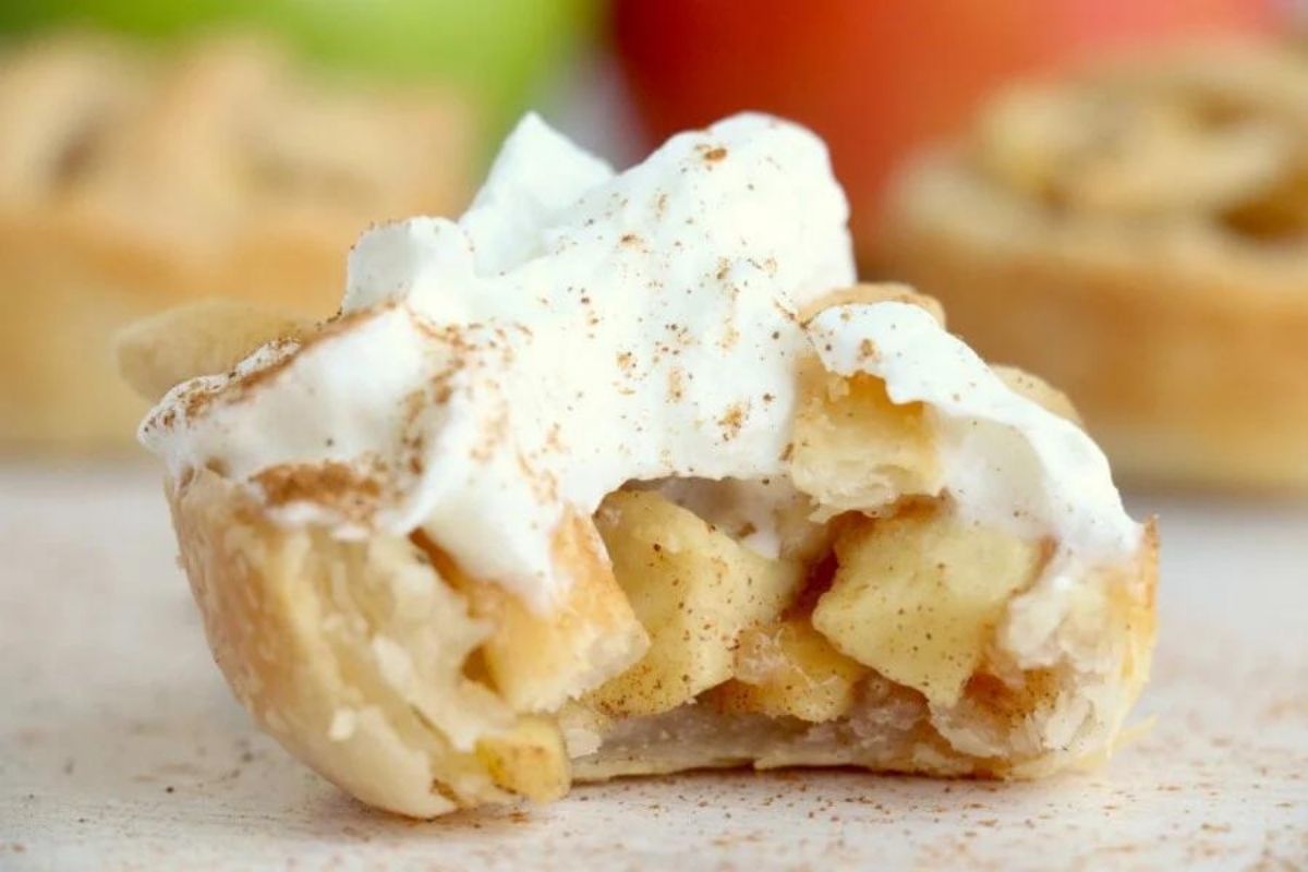 A close-up of a slice of apple pie topped with whipped cream and a sprinkle of cinnamon from our Pie Recipes collection.