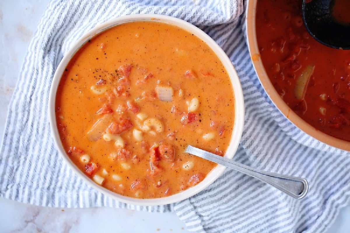A bowl of creamy tomato soup with pasta and chunks of vegetables on a striped cloth, inspired by recipes from grandma.