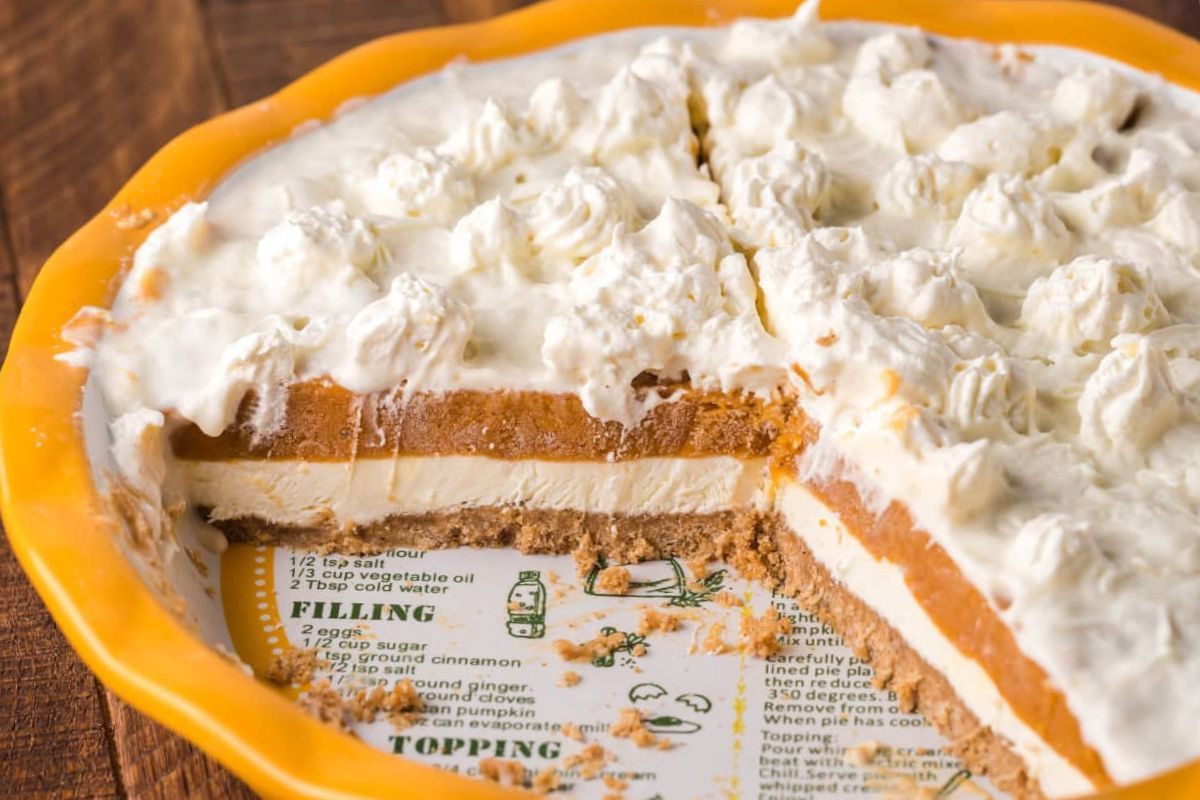 A pumpkin pie with whipped cream topping, partially sliced, on a pie recipes-printed plate.
