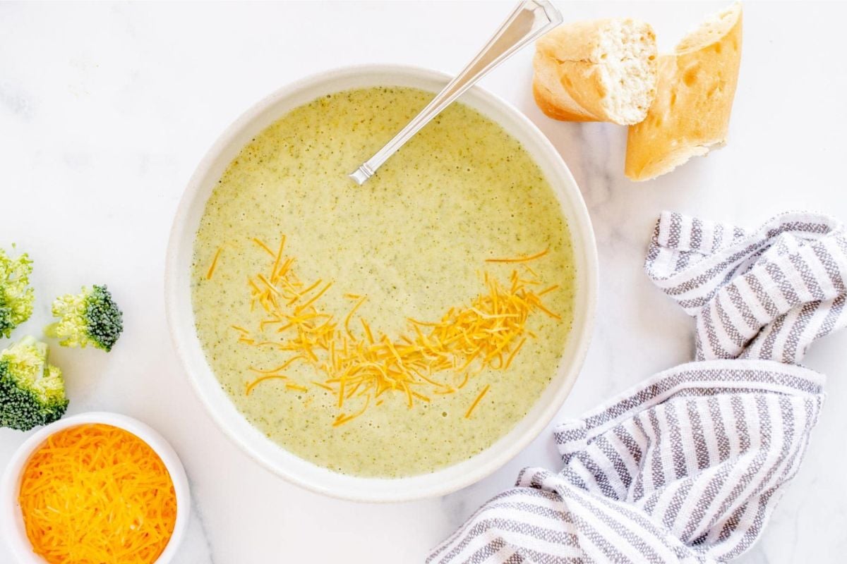 A bowl of broccoli soup recipes with cheese and bread.