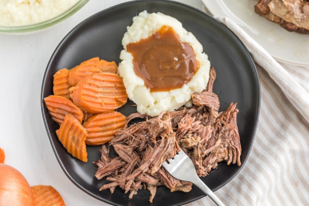 A plate of old-fashioned pulled beef with mashed potatoes, gravy, and sliced carrots.