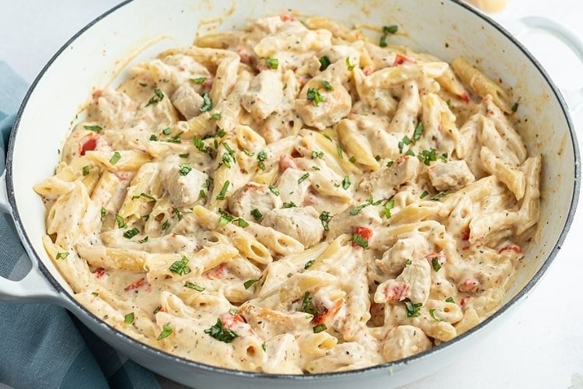 Creamy penne pasta with chicken and herbs in a white skillet, garnished with chopped parsley—a must-try for fans of cheesy recipes.
