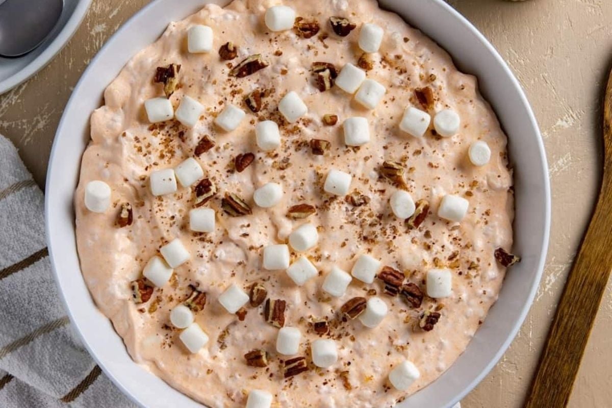 A white bowl with marshmallows, pecans, and jello salads in it.