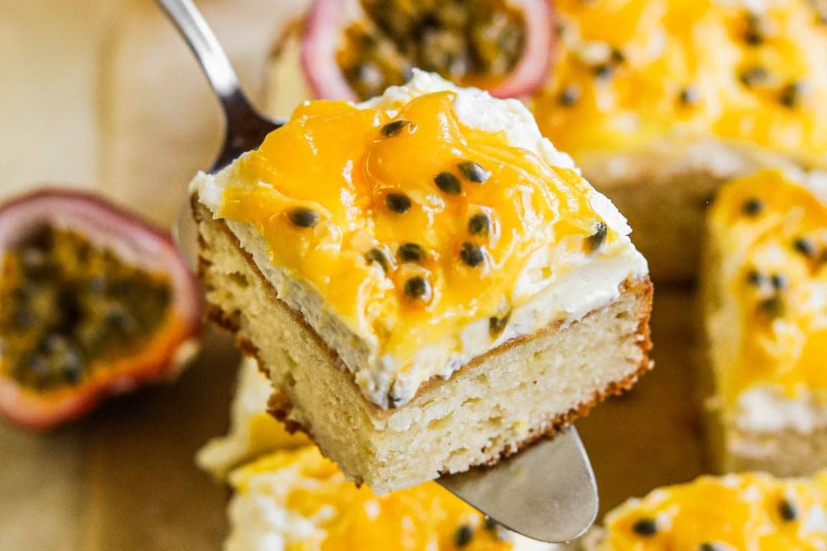 A slice of Easter cake topped with cream and passion fruit pulp on a fork, with more cake pieces and halved passion fruits in the background.