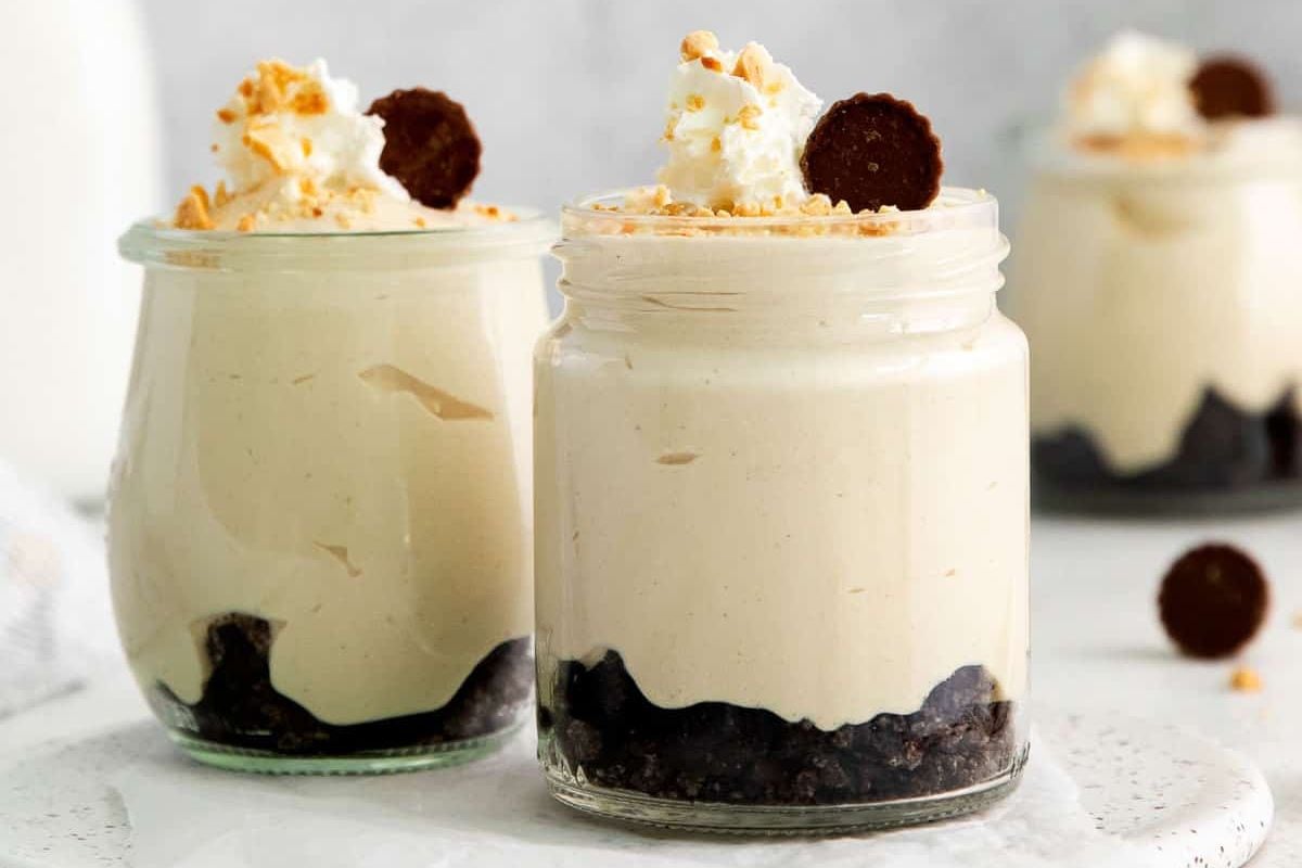 Two jars of creamy, single-serve individual desserts with a cookie crust, topped with whipped cream, a cookie, and crumbs.