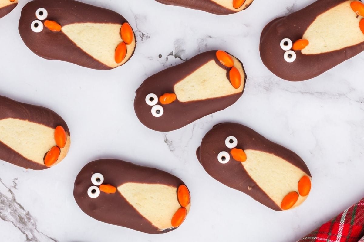 Cookies decorated to look like penguins with chocolate coating and candy eyes on a marble surface, inspired by unique cookie recipes.