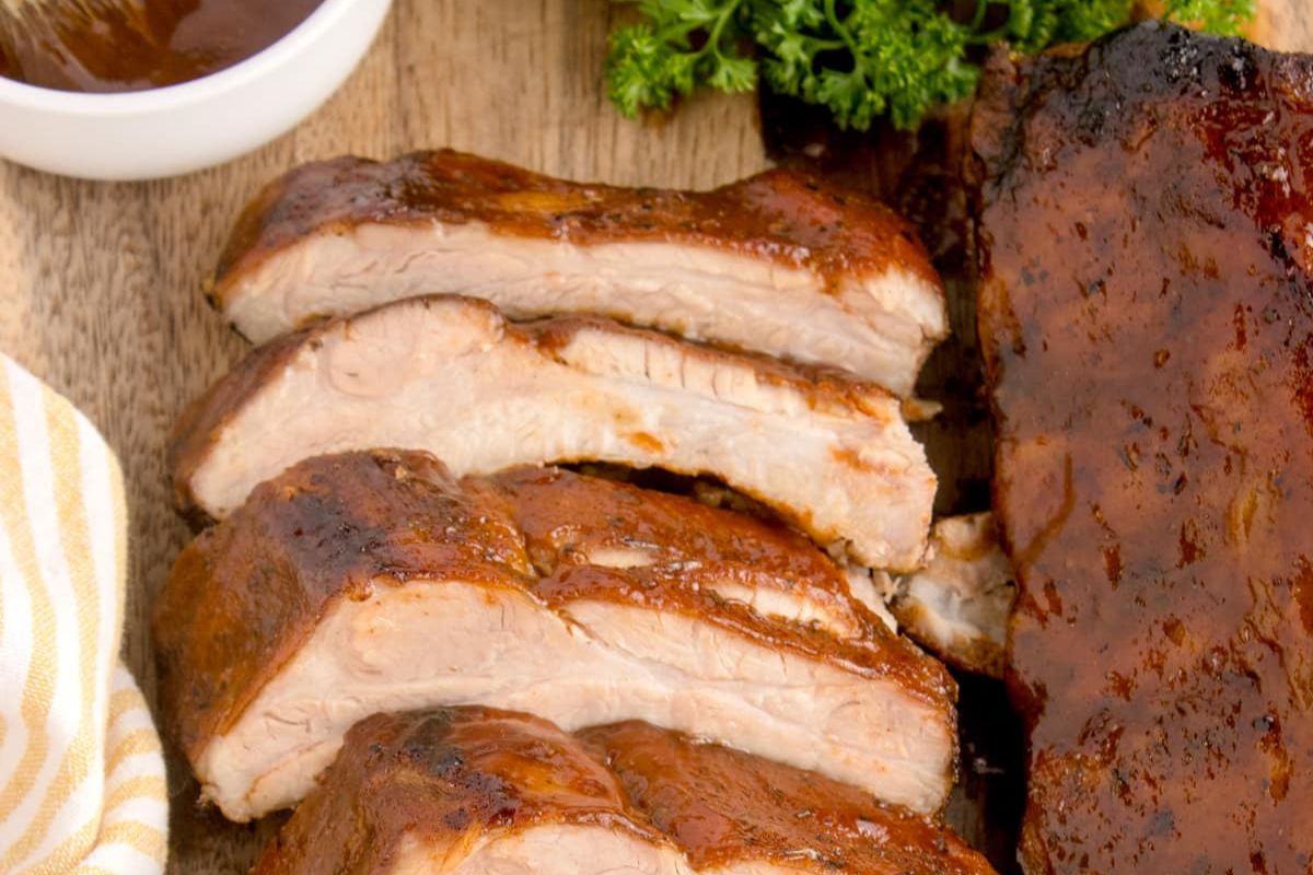 Easy rib recipes: Sliced barbecue pork ribs on a wooden cutting board with sauce on the side.