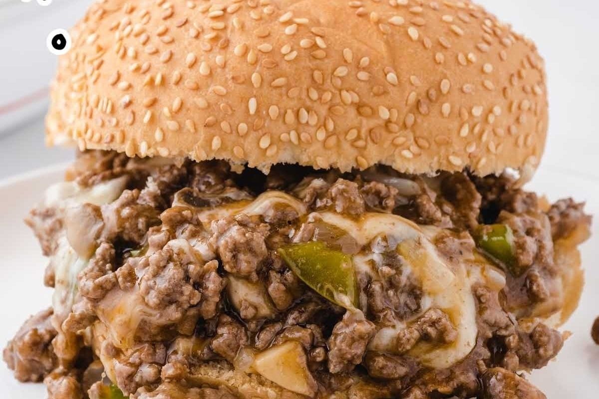 Close-up of a cheesy sloppy joe sandwich with ground beef, onions, and bell peppers, topped with melted cheese on a sesame seed bun.