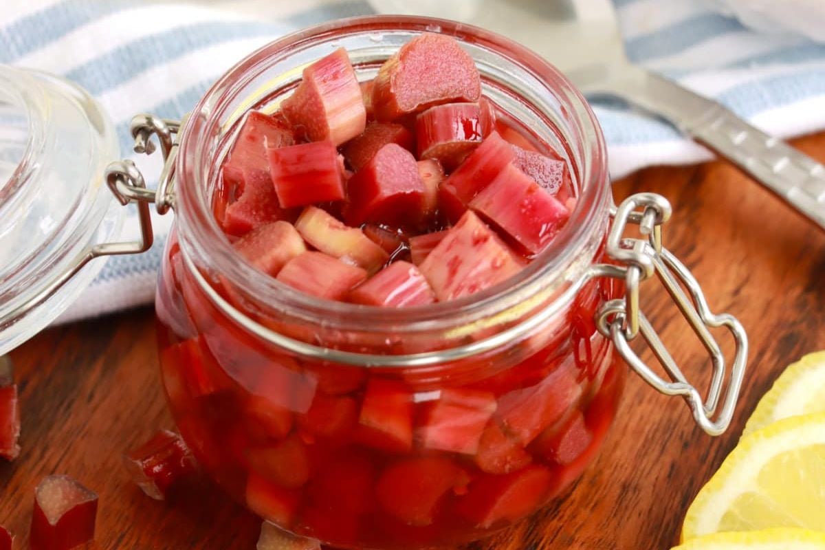 A jar of pickled rhubarb with lemon slices and useful rhubarb recipes in the background.